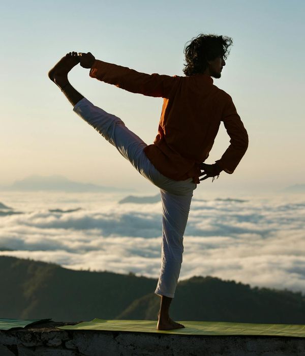Silhouette of a person in a powerful yoga warrior pose at sunrise.